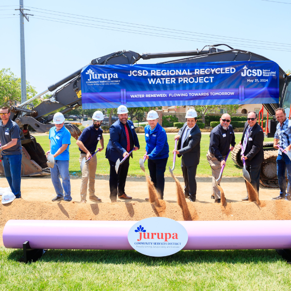 Group with hard hat and shovels stand over purple pipe